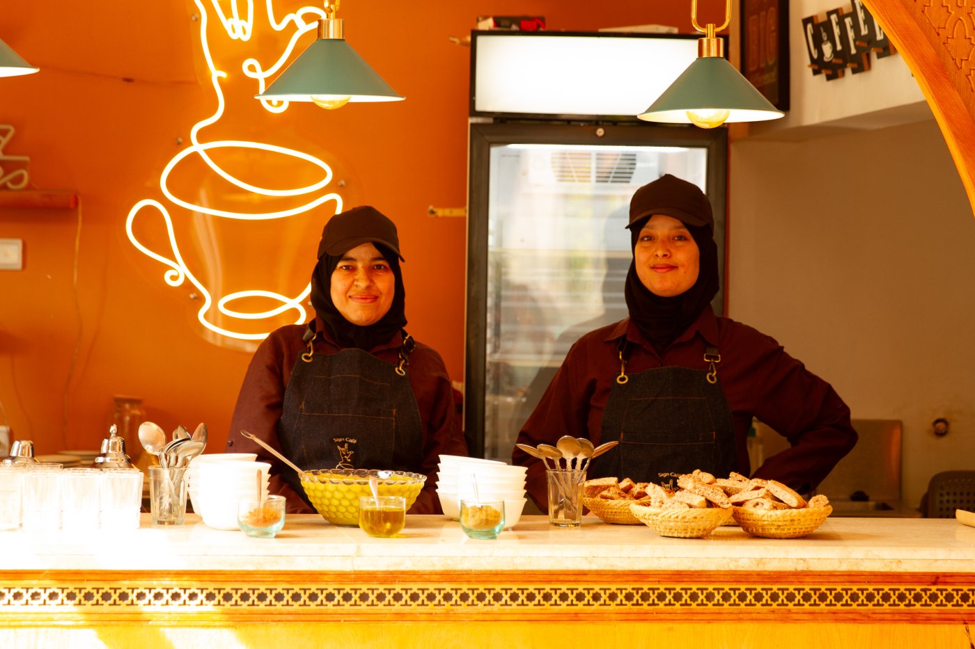 Sign Café baristas at the counter under the neon sign